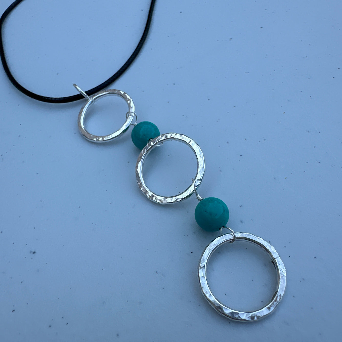 Three circle rings and turquoise pendant on simple lace