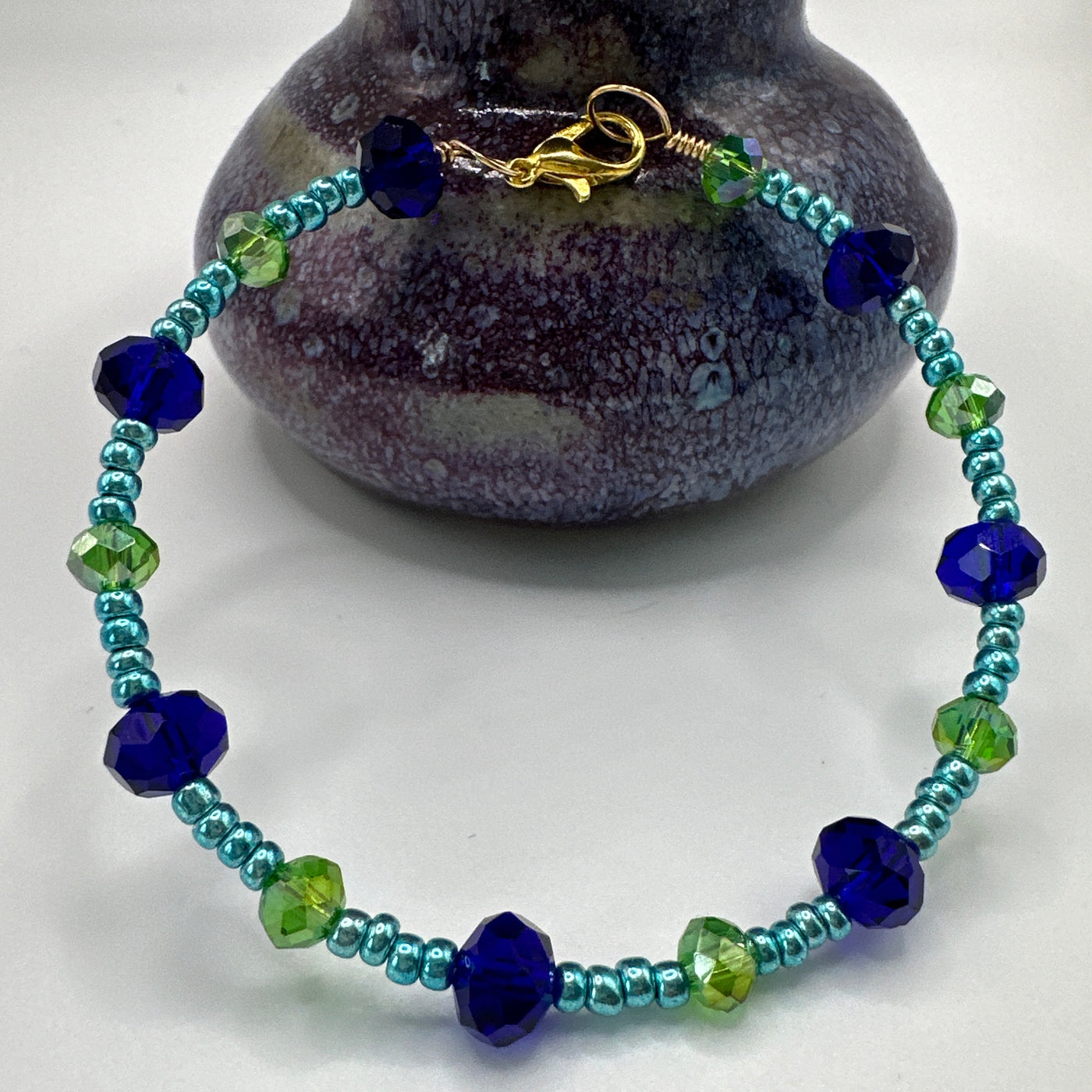 Rigid bracelet with blue and green faceted glass and metallic blue pearls