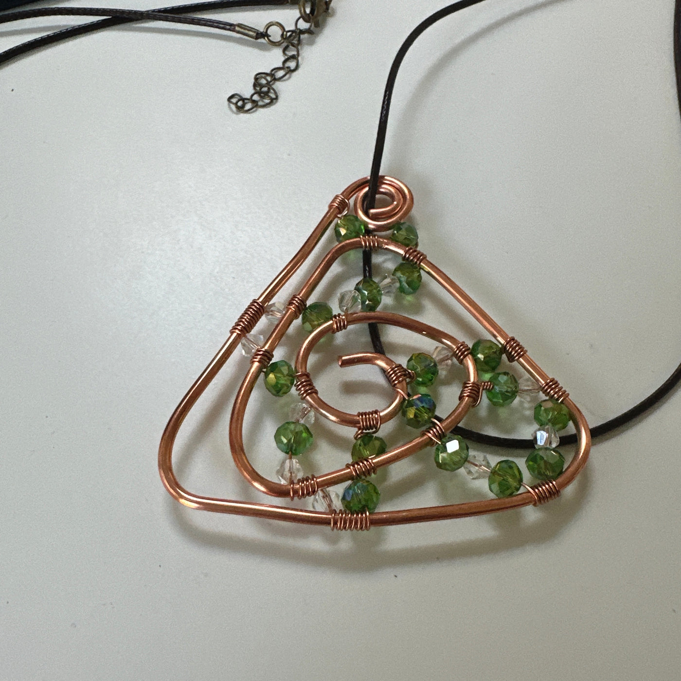 Copper abstract triangle design with green and white chrystals. Leather cord