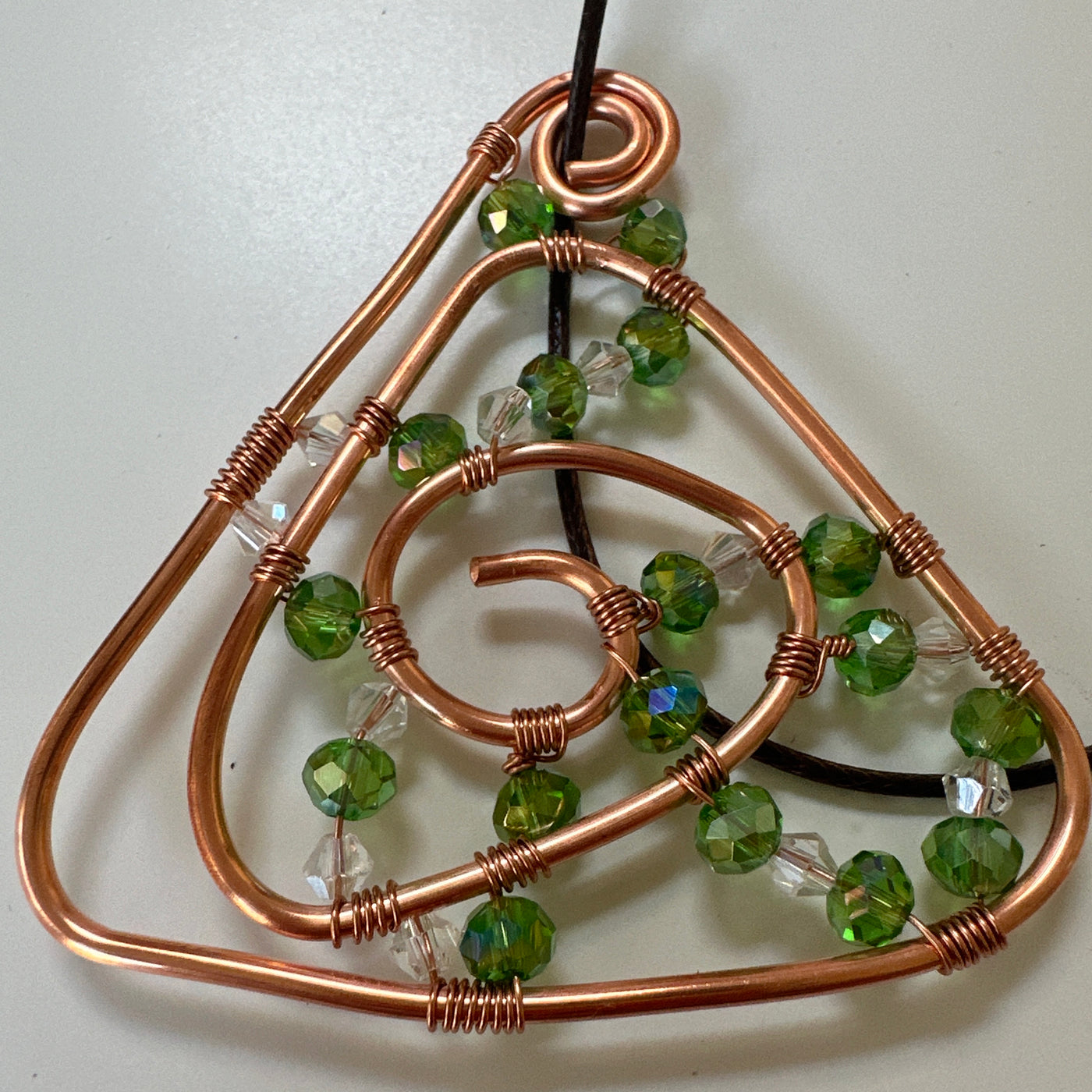 Copper abstract triangle design with green and white chrystals. Leather cord