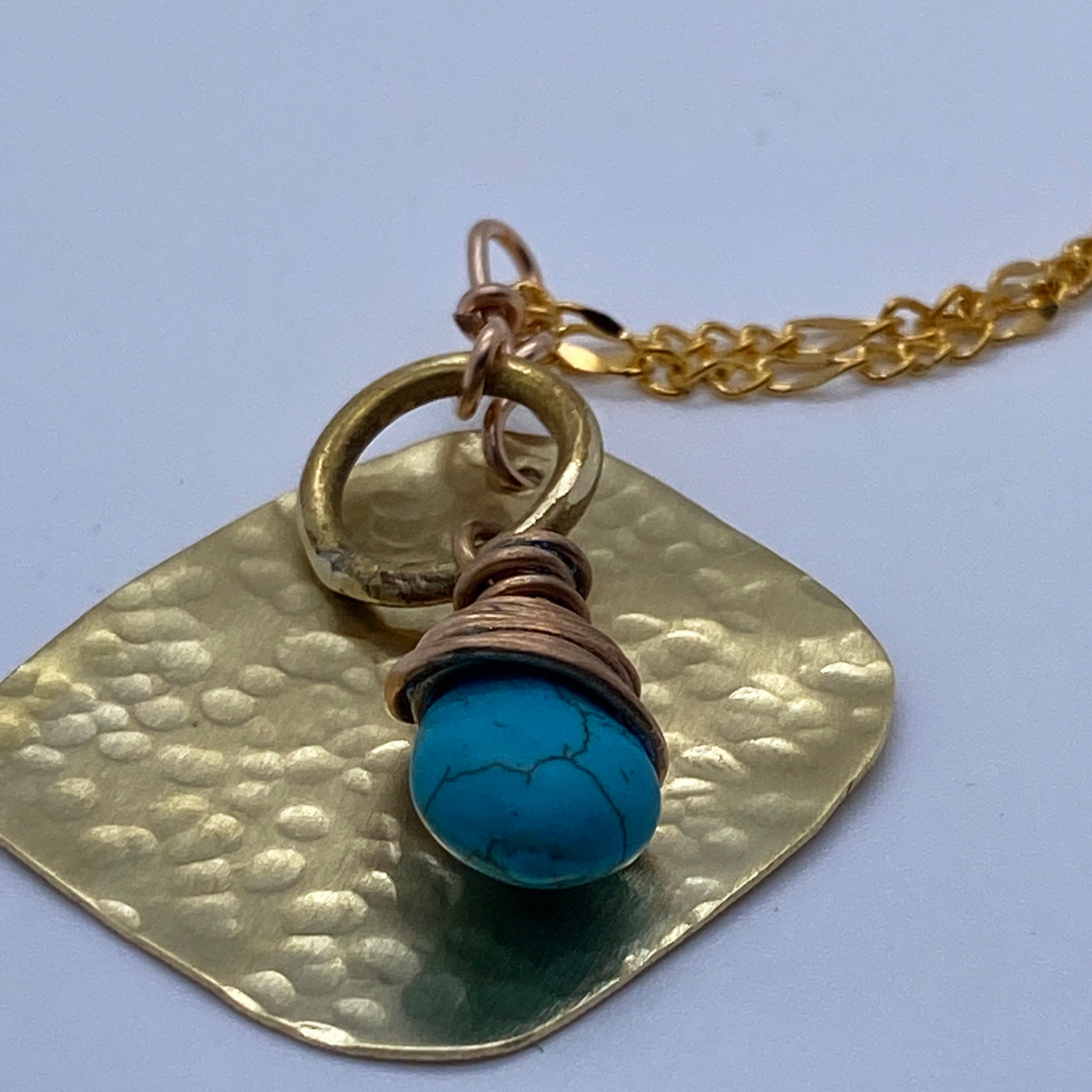 Turquoise pending from a brass circle and square.