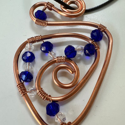 Copper abstract triangle design with blue and white chrystals. Leather cord