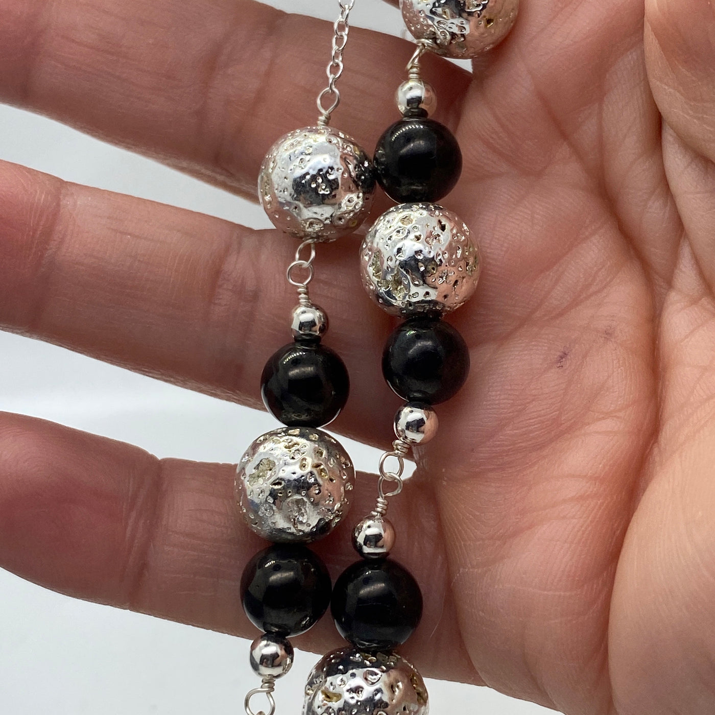 Silberne Lavasteinperlen und tiefschwarze 8-mm-Perlen an einer Kette.