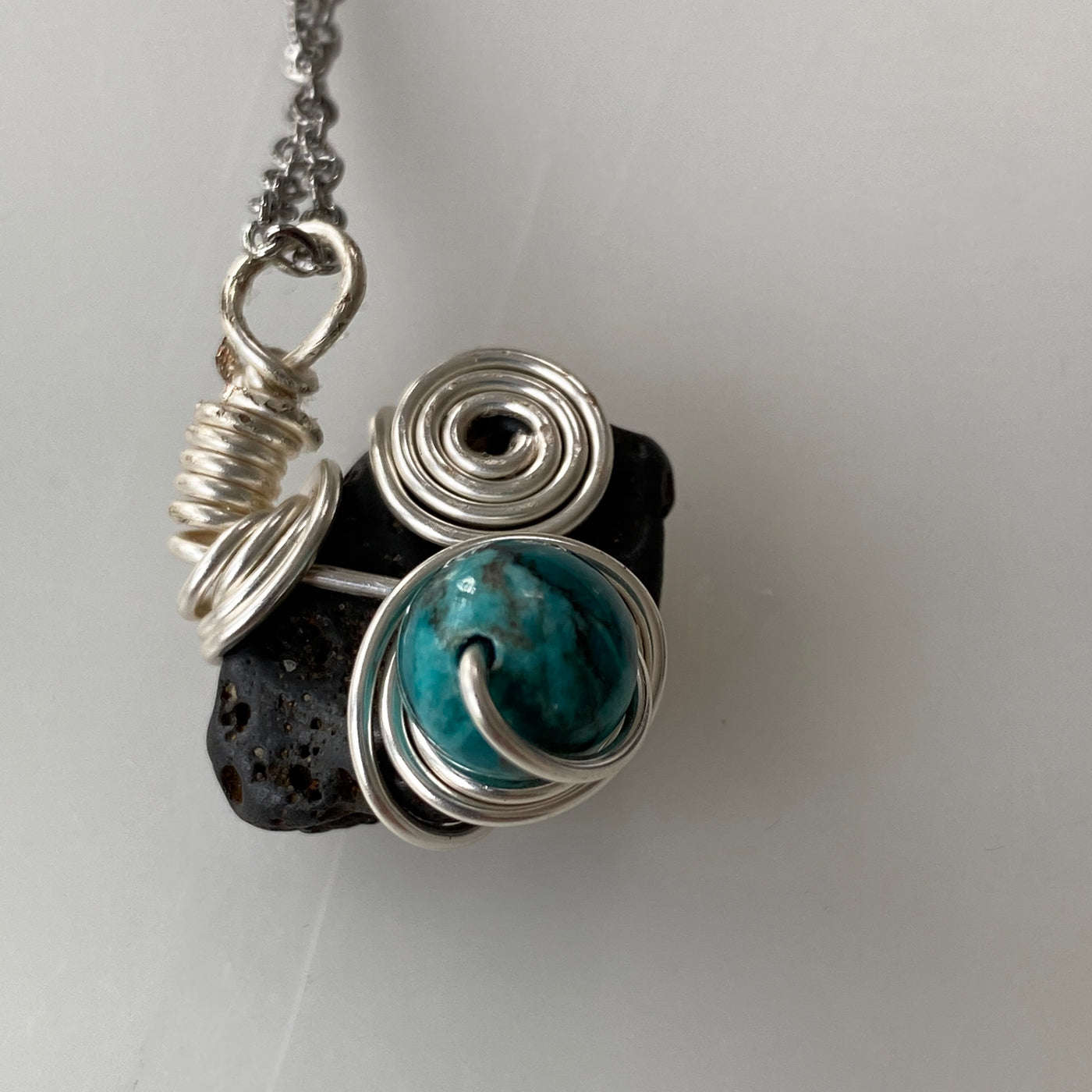 Small pendant featuring a grey natural stone, turquoise and silver wire. Elbastones collection.